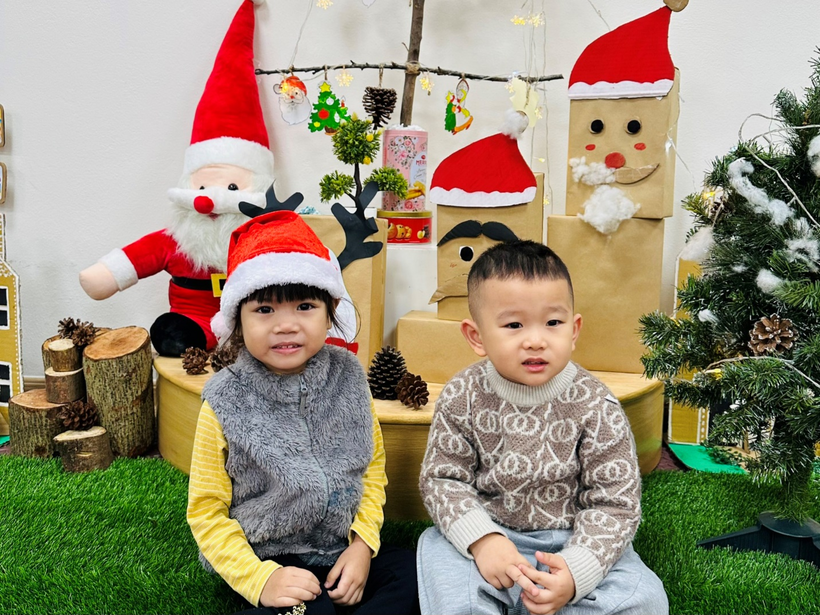 Two children sitting in front of a christmas decoration

Description automatically generated